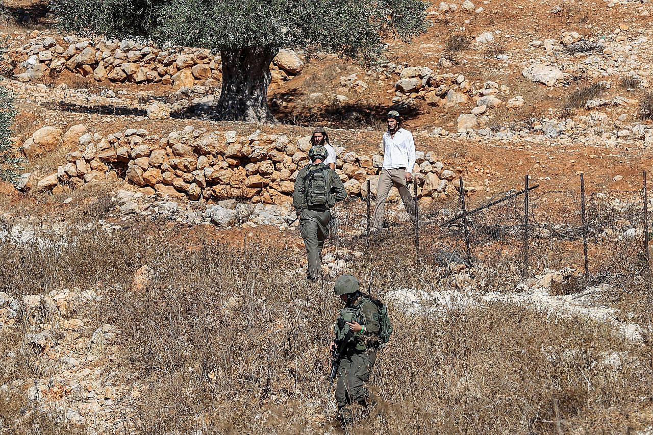 Se ve a colonos judíos y soldados israelíes observando a agricultores palestinos y activistas de izquierda mientras recogen aceitunas durante la temporada de cosecha anual, en la aldea de Burqa, al este de Ramallah, Cisjordania ocupada, el 20 de octubre de 2024. (Flash90)